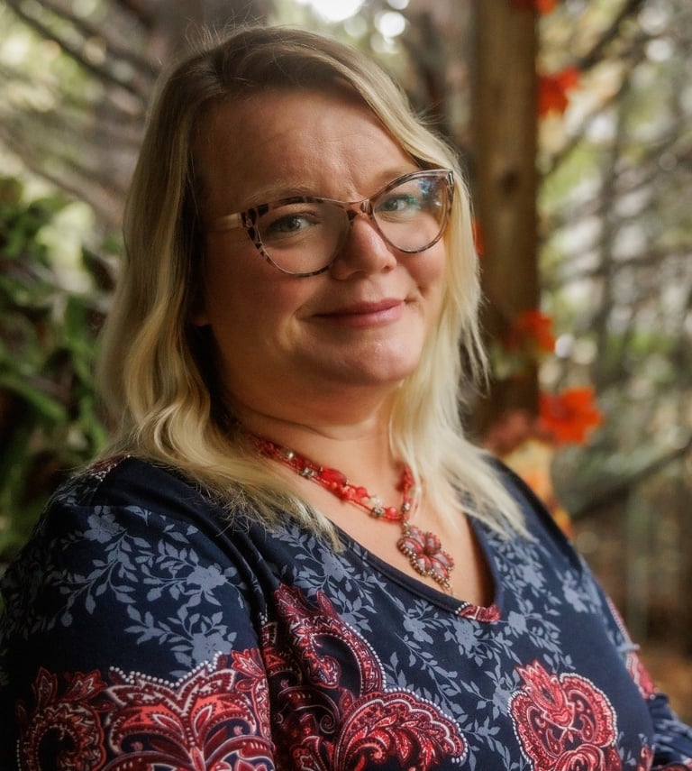 Middle age woman standing comfortably on her deck and looking toward the camera.