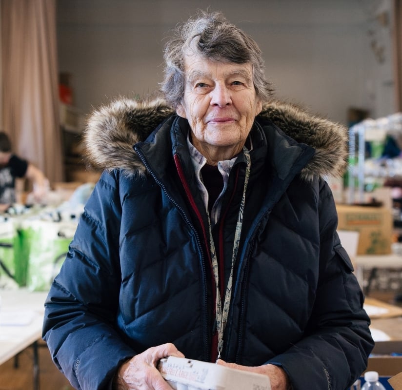 Senior woman standing in the center of a food pantry holding eggs